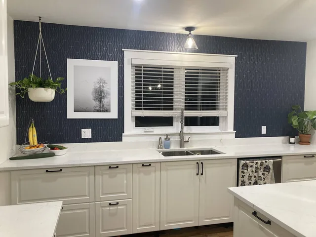 White kitchen cabinets and sink below a window with a dark feature wall